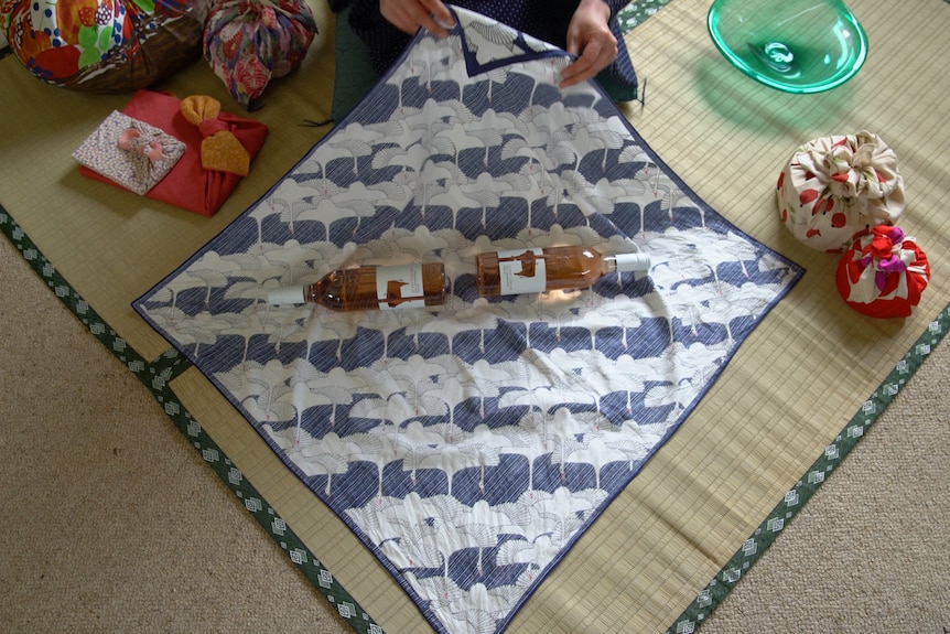 Two wine bottles facing opposite ends in the middle of a dark blue and white furoshiki fabric