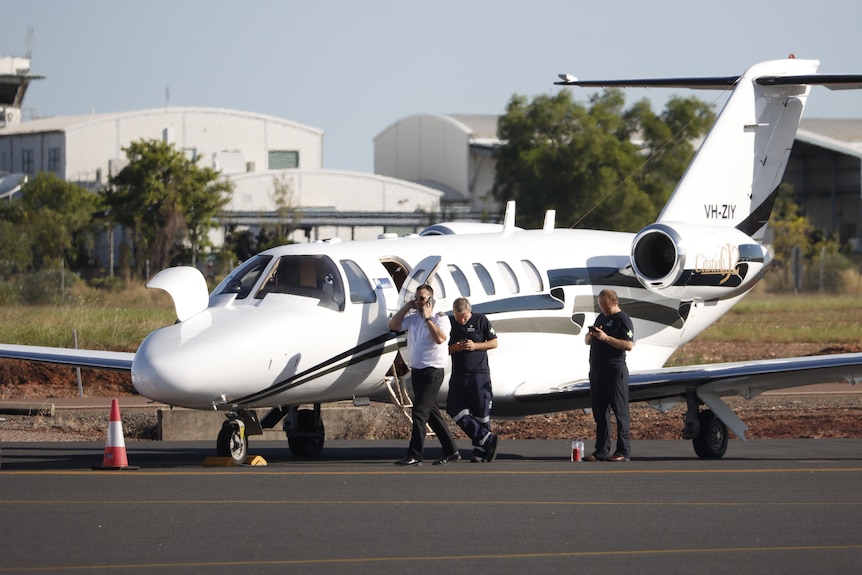 A small plane sitting on tarmac with people standing outside it