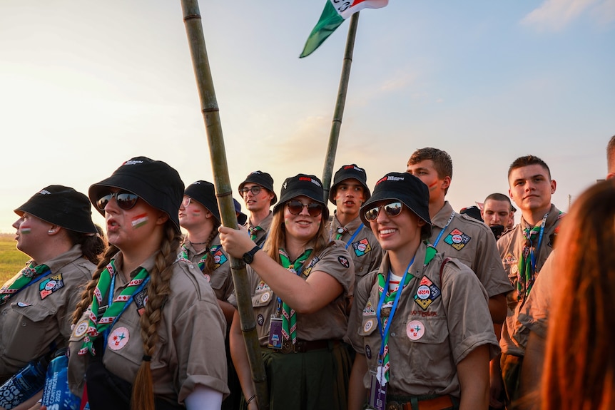 A dozen young people in scout uniform hold a country flag and walk as they walk