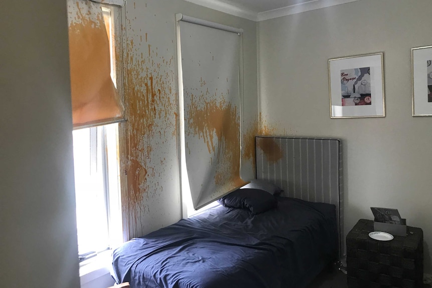Orange paint is seen splashed on the wall of a bedroom.