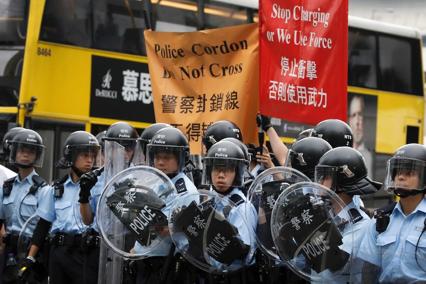 Police in riot gear near signs saying 'stop charging or we use force'.