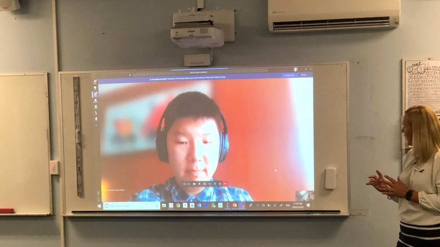 A child's image is projected onto a whiteboard. It looks like a livestream. A woman seems to be speaking to him.