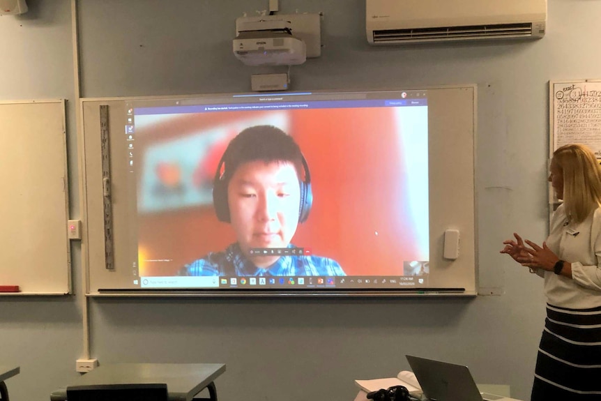 A child's image is projected onto a whiteboard. It looks like a livestream. A woman seems to be speaking to him.