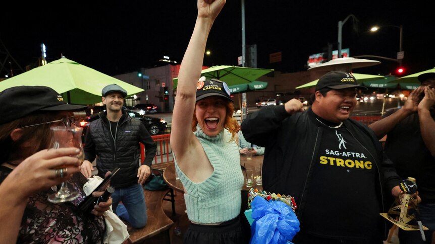 Woman in sag-aftra cap and green shirt pumps fist in air 