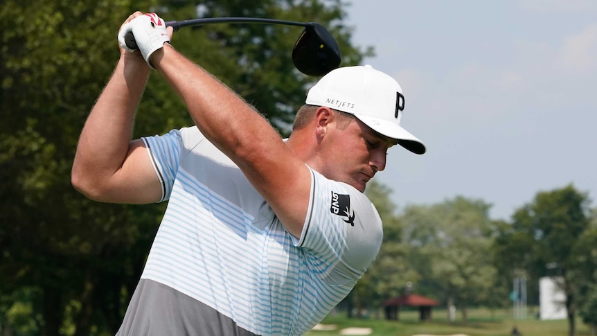 A golf club bends in the hands of a golfer at the top of his backswing before a tee shot.