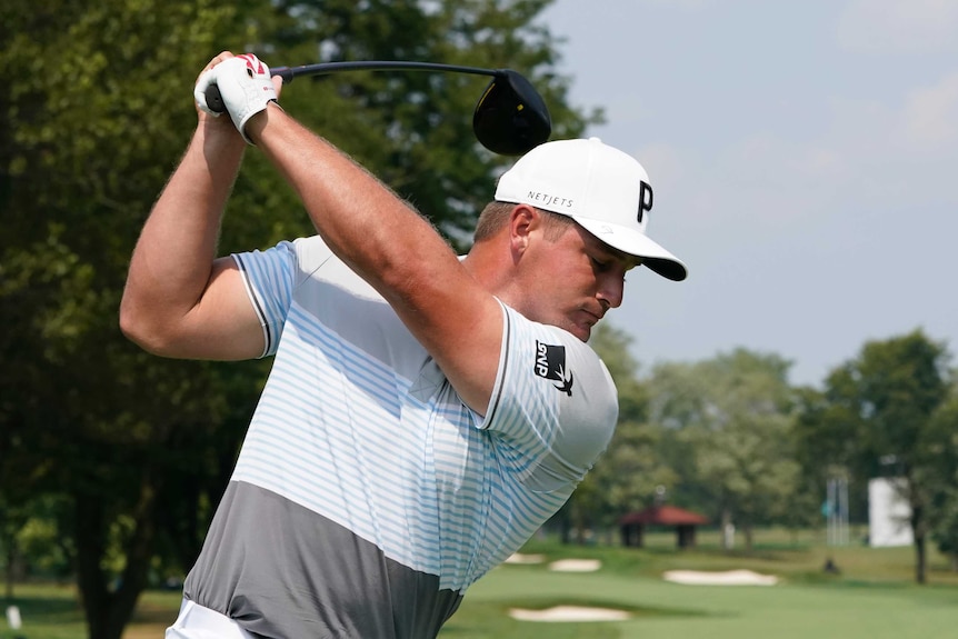 A golf club bends in the hands of a golfer at the top of his backswing before a tee shot.