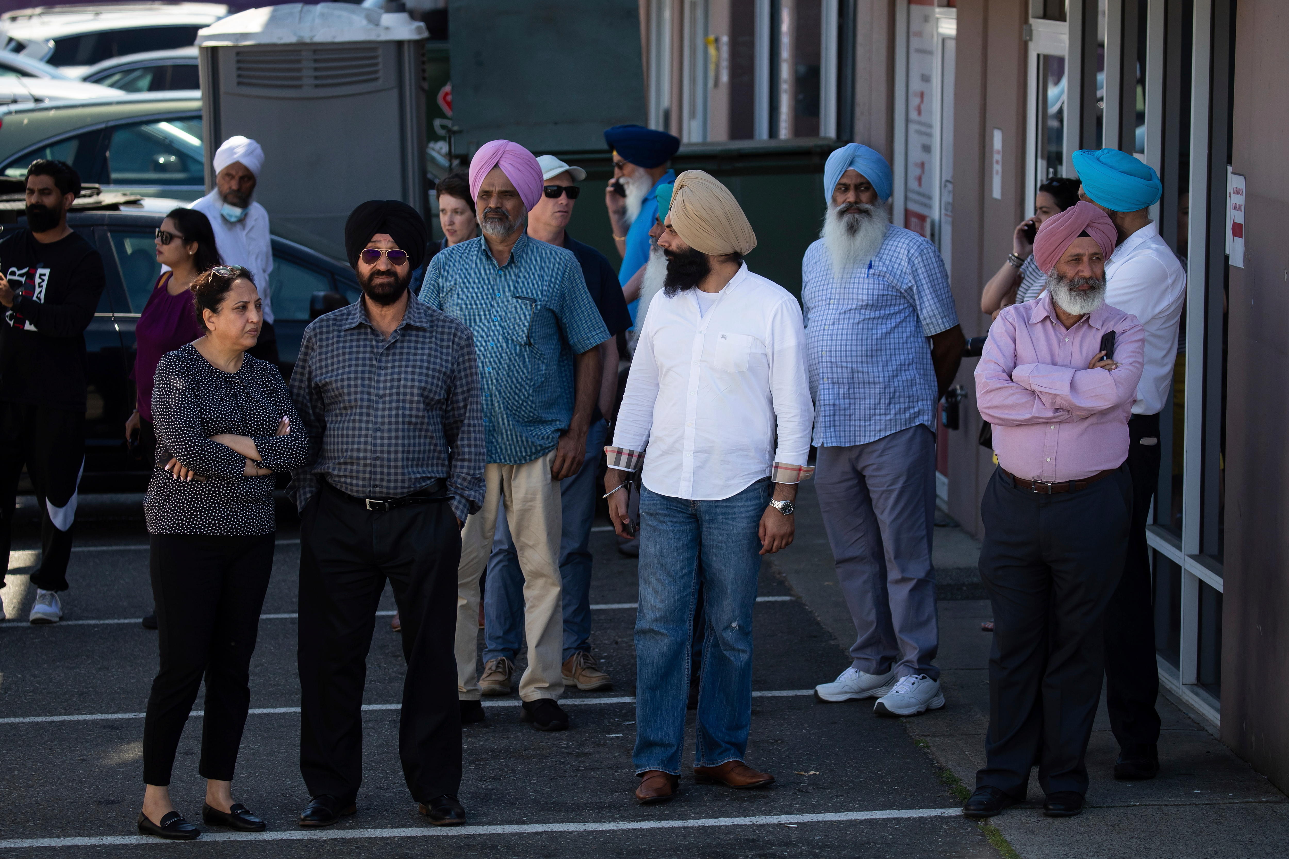 A group of people stand around outside a building near the crime scene of Ripudaman Singh Malik's shooting. 