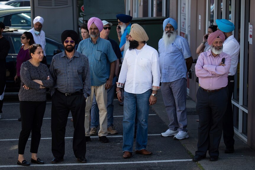 A group of people stand around outside a building near the crime scene of Ripudaman Singh Malik's shooting. 