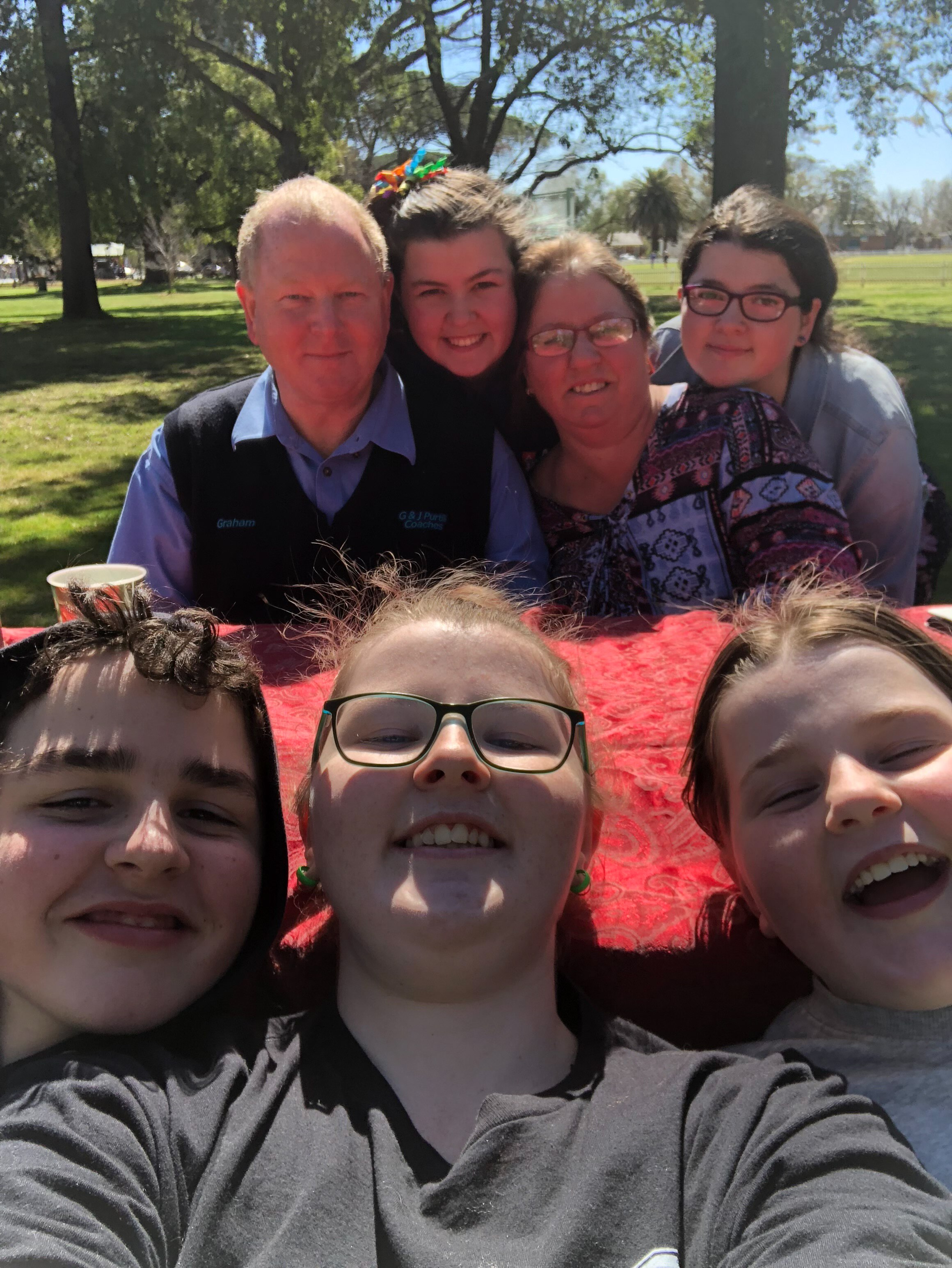 Family of two adults and five children smiles at camera outdoors.