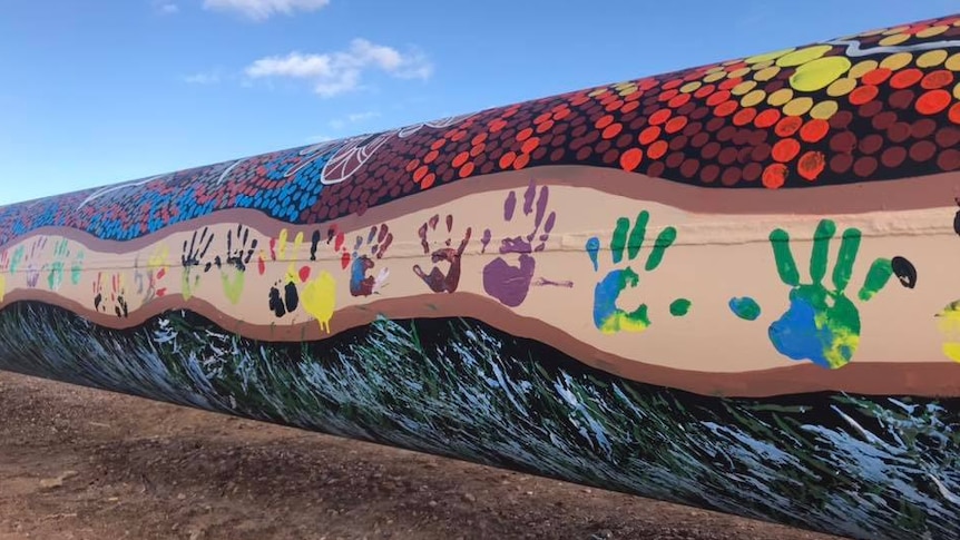 A large pipeline painted black with red, orange and yellow dots as well as colourful handprints.