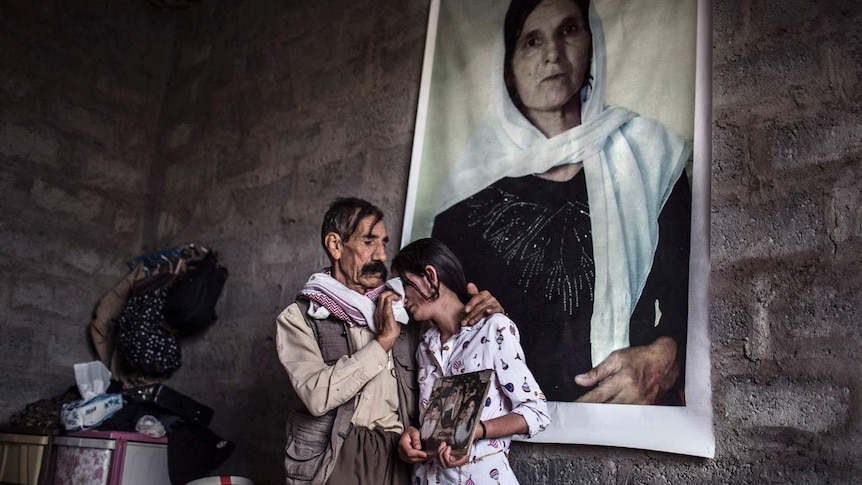 An Iraqi father comforts his daughter as they stand in front of a portrait of their slain wife and mother.