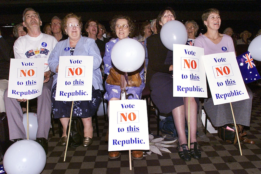 A group of men and women hold signs saying 'vote no to this republic'.