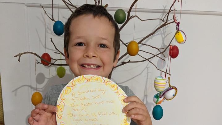 Phoenix Mapham holds up a piece of paper with writing on it while standing in front of an Easter tree.