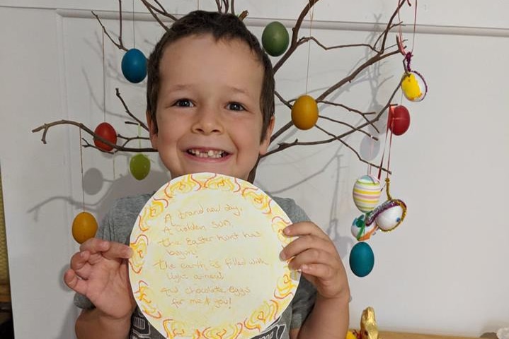 Phoenix Mapham holds up a piece of paper with writing on it while standing in front of an Easter tree.