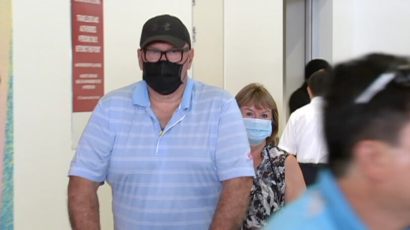 A man and a woman wearing face masks push a luggage trolley