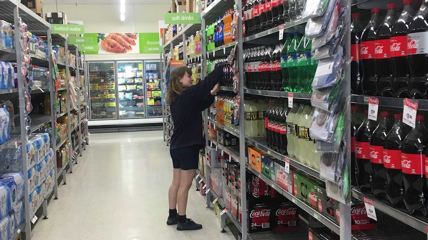 A supermarket assistant stacks shelves with bottled drinks