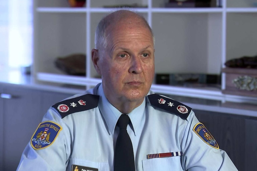 A man in a blue uniform sitting in a white room.