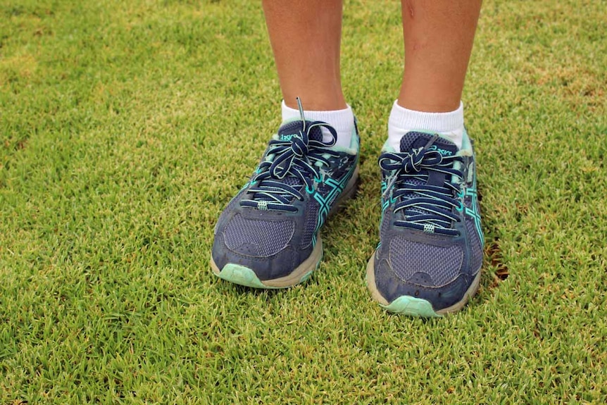 A pair of child's feet in shoes photographed standing on green grass.