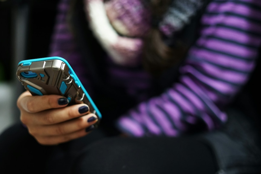Arms of woman in purple long-sleeved top using mobile phone with blue and grey case.