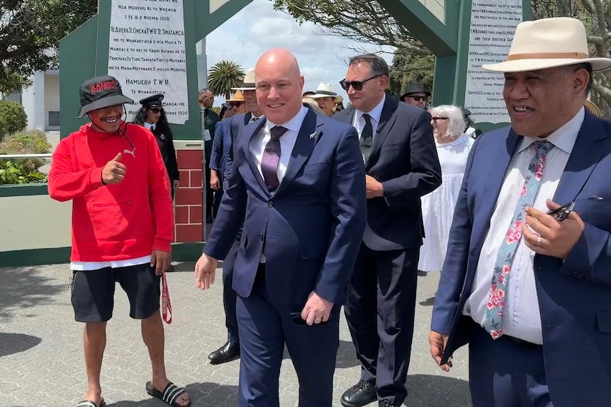 The Prime Minister wears a suit and walks through the gates at the Maori church 