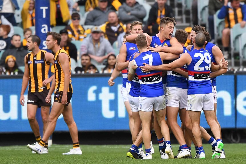 A group of AFL players surround the goalscorer, as their dejected opponents walk away.