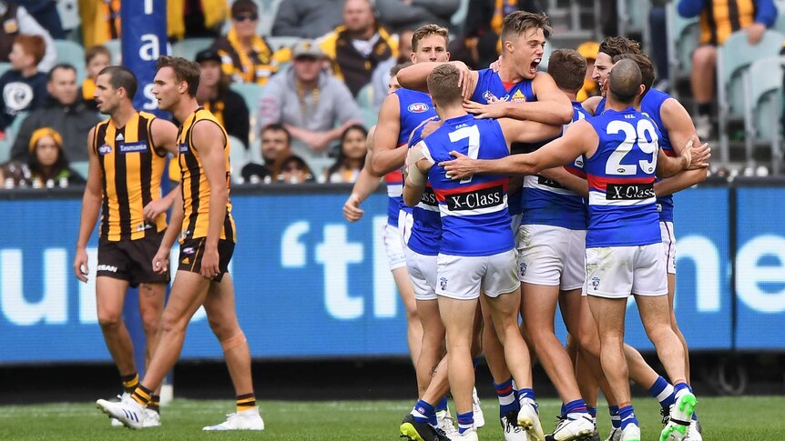 A group of AFL players surround the goalscorer, as their dejected opponents walk away.