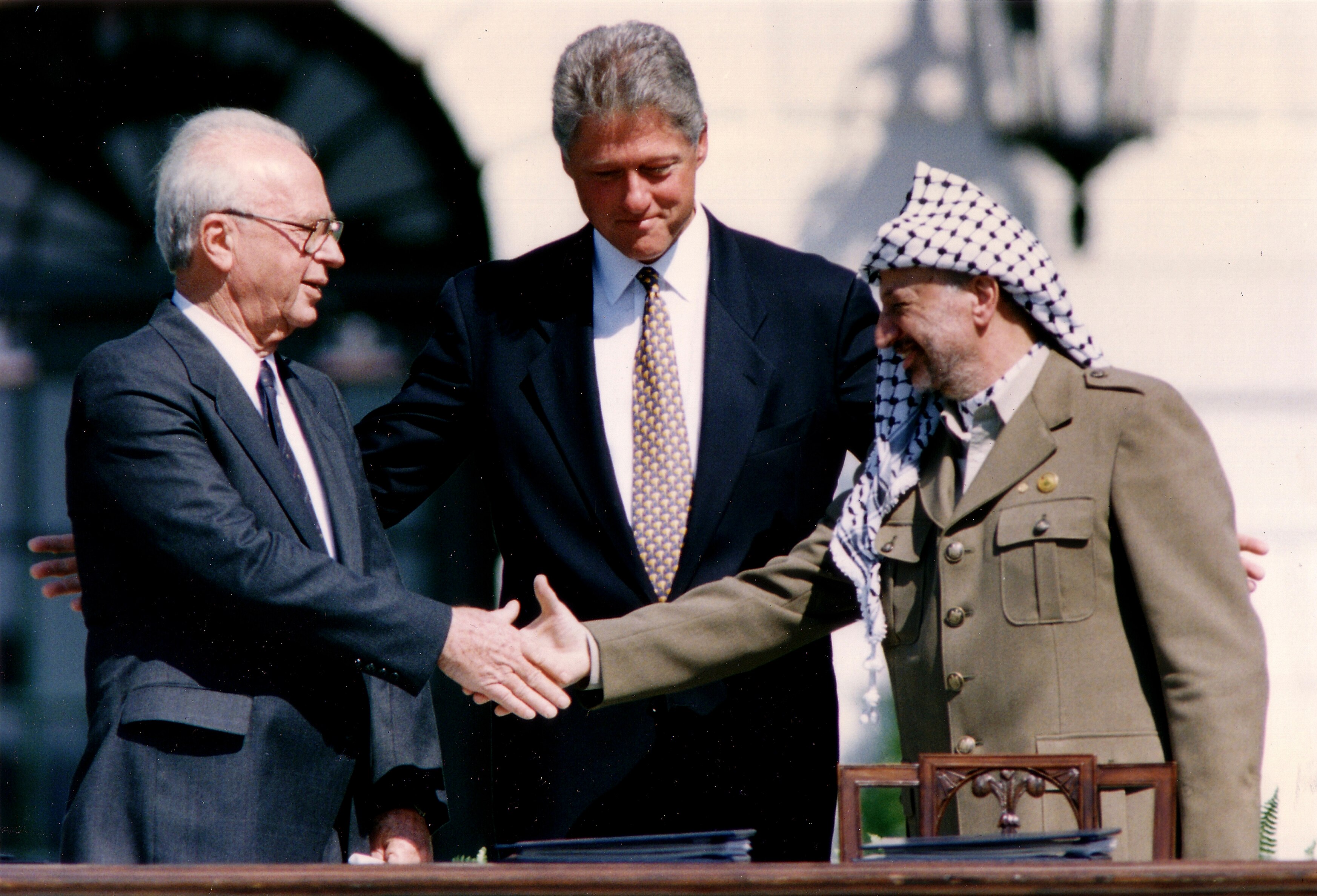 Yitzhak Rabin and Yasser Arafat shake hands as Bill Cliton stands behind them.