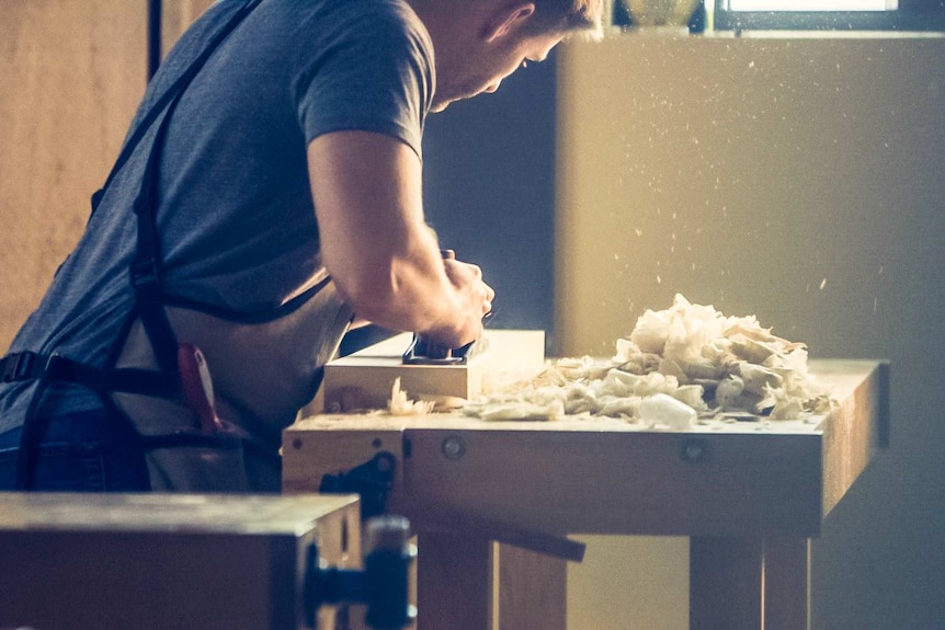 A man sanding a table with his back to the camera