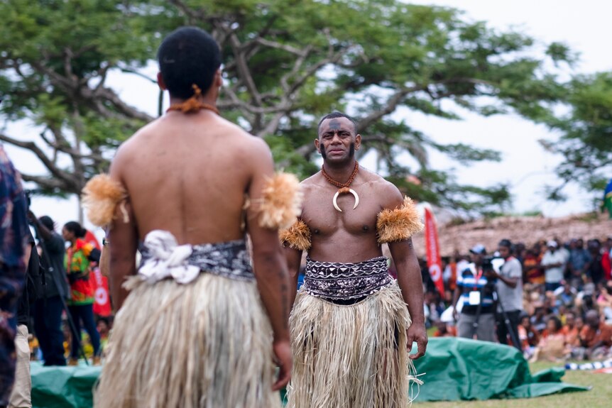 Fijian men in traditional woven skirts perform meke in black face markings