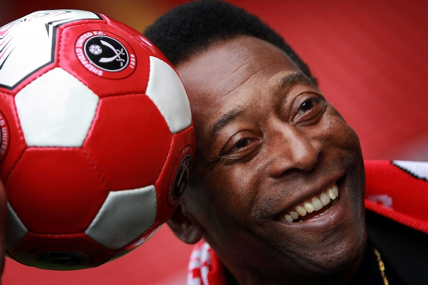 Former Brazilian national footballer Pele holds a soccer ball against his head