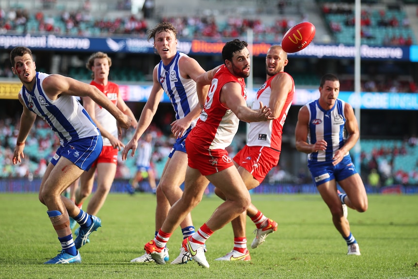 A Sydney AFL defender reaches out with his eyes on the ball, as a group of opposing players turn and watch him take possession.