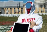 A dummy in a white sweatshirt and a mirror for a face sits at a school desk in a circle of roses on the US capitol lawn.