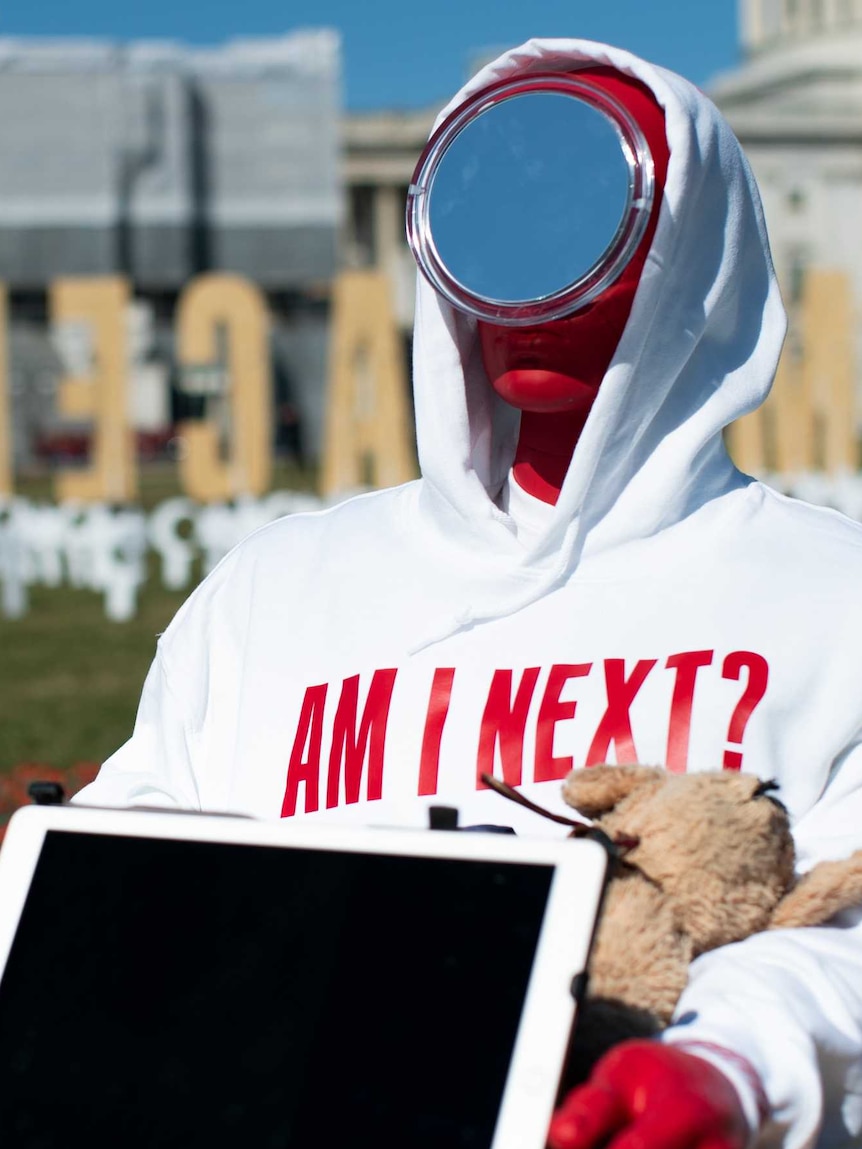 A red dummy wears a T-shirt saying "Am I next?" and has a mirror for a face.
