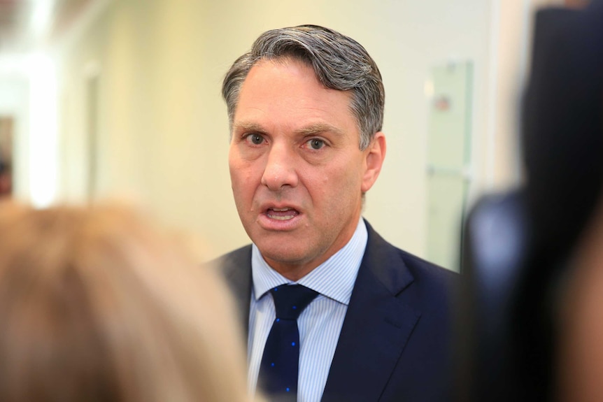 A man wearing a dark suit talks to reporters.