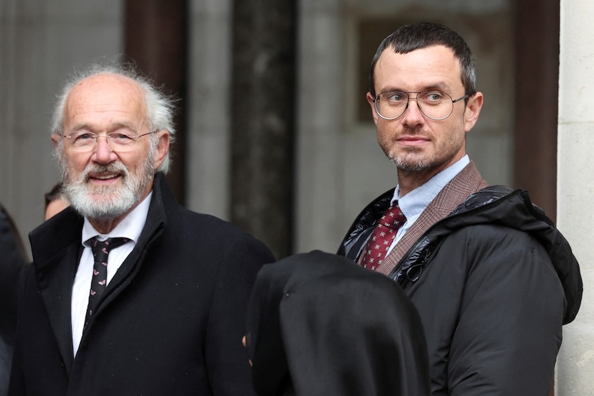 Two men in suits with neutral expressions looking on