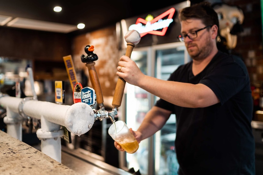 A close-up shot of a hand holding a full pint of beer below a beer tap after pouring it at a bar in a pub.