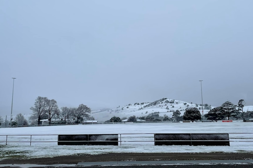 A country football oval and hills in the background covered in snow. 