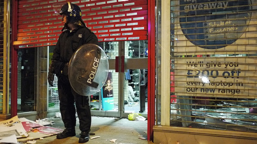 A police officer stands guard outside a looted store in Clapham Junction