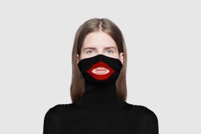 A model wears a black jumper pulled over her nose, with a large red-ringed hole around her mouth.