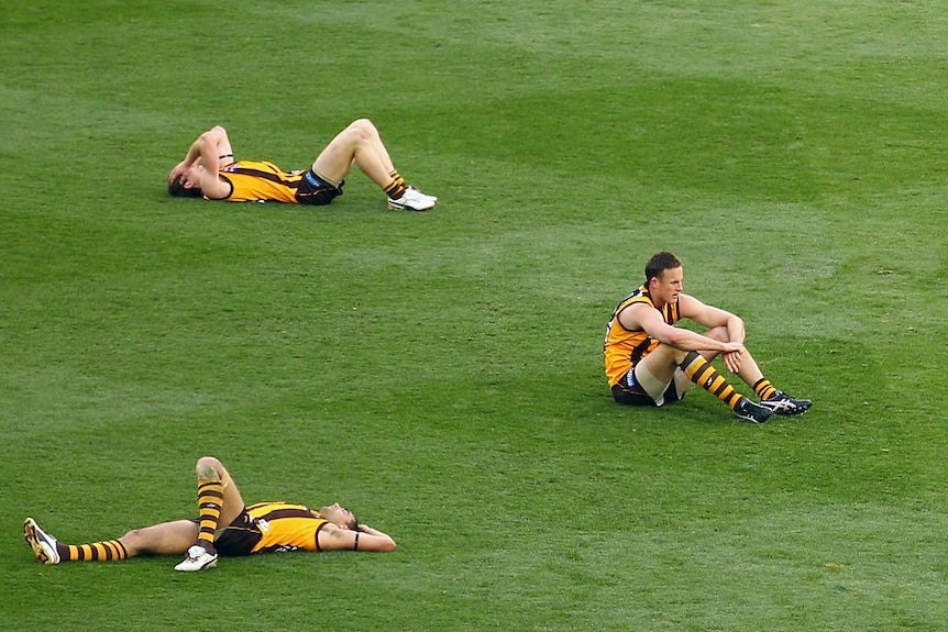 Hawthorn players lie on the MCG after losing the 2012 AFL grand final to the Sydney Swans.