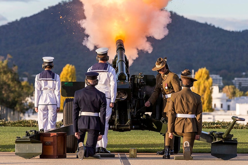 soldiers stand with their backs to camera firing a howitzer outside Parliament House