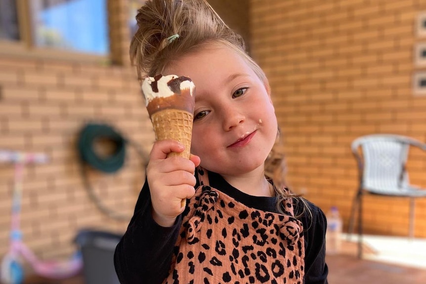 Cleo Smith stands on a patio smiling and holding up an ice cream cone.