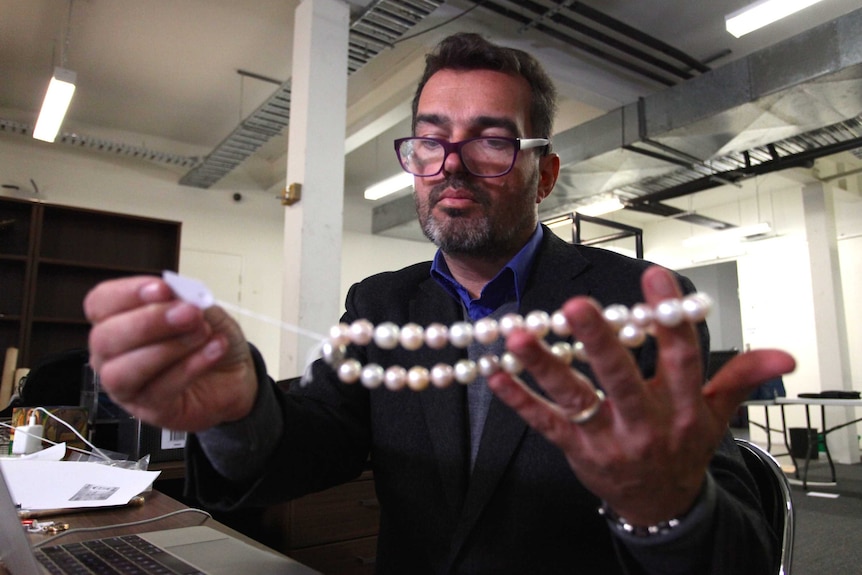 Paul Sumner holds a tag while examining a pearl necklace.