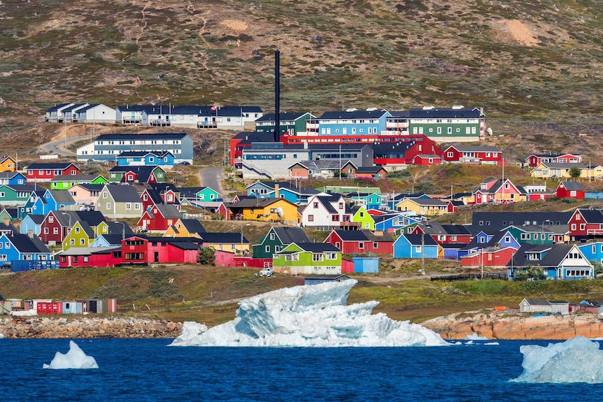 Colourful houses sit close near the ocean. Ice and water in the foreground.