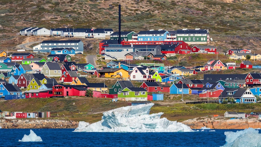 Colourful houses sit close near the ocean. Ice and water in the foreground.