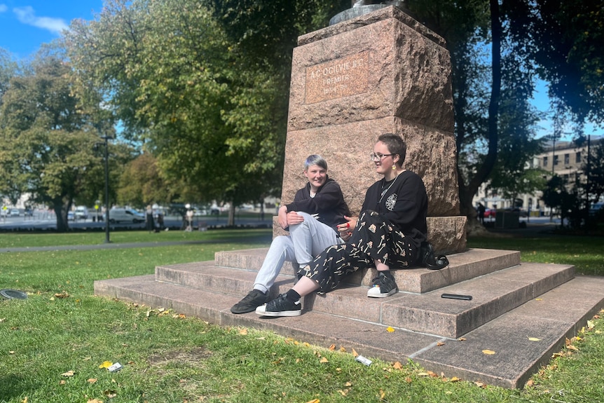 Kelly and Eve sit next to each other at the base of a statue in a park