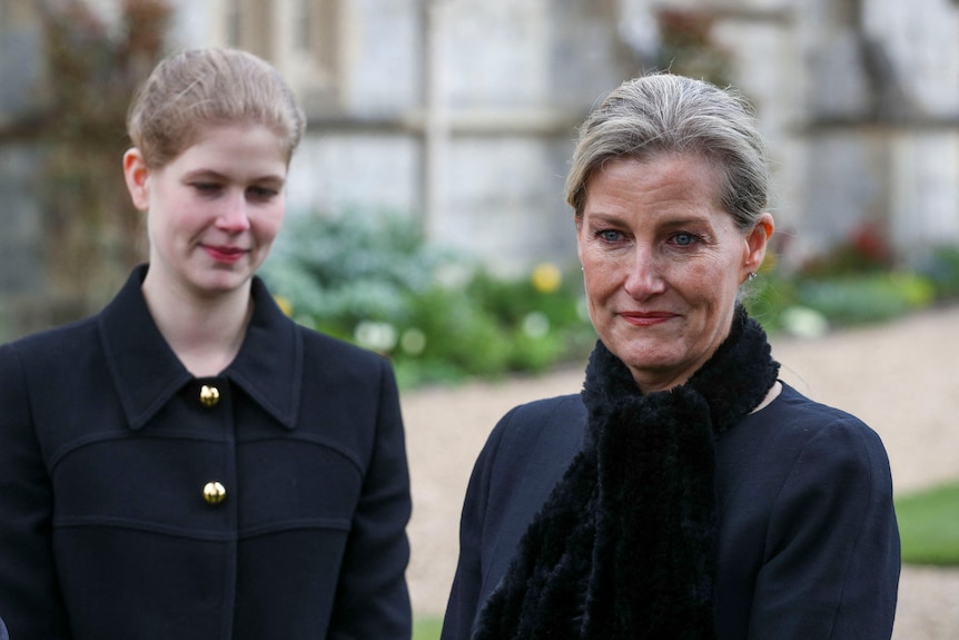 Sophie looks past the camera, her daughter stands behind her. 