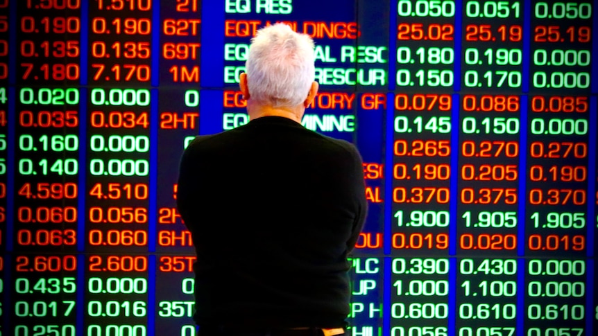 A stock market watcher stands in front of an ASX board.