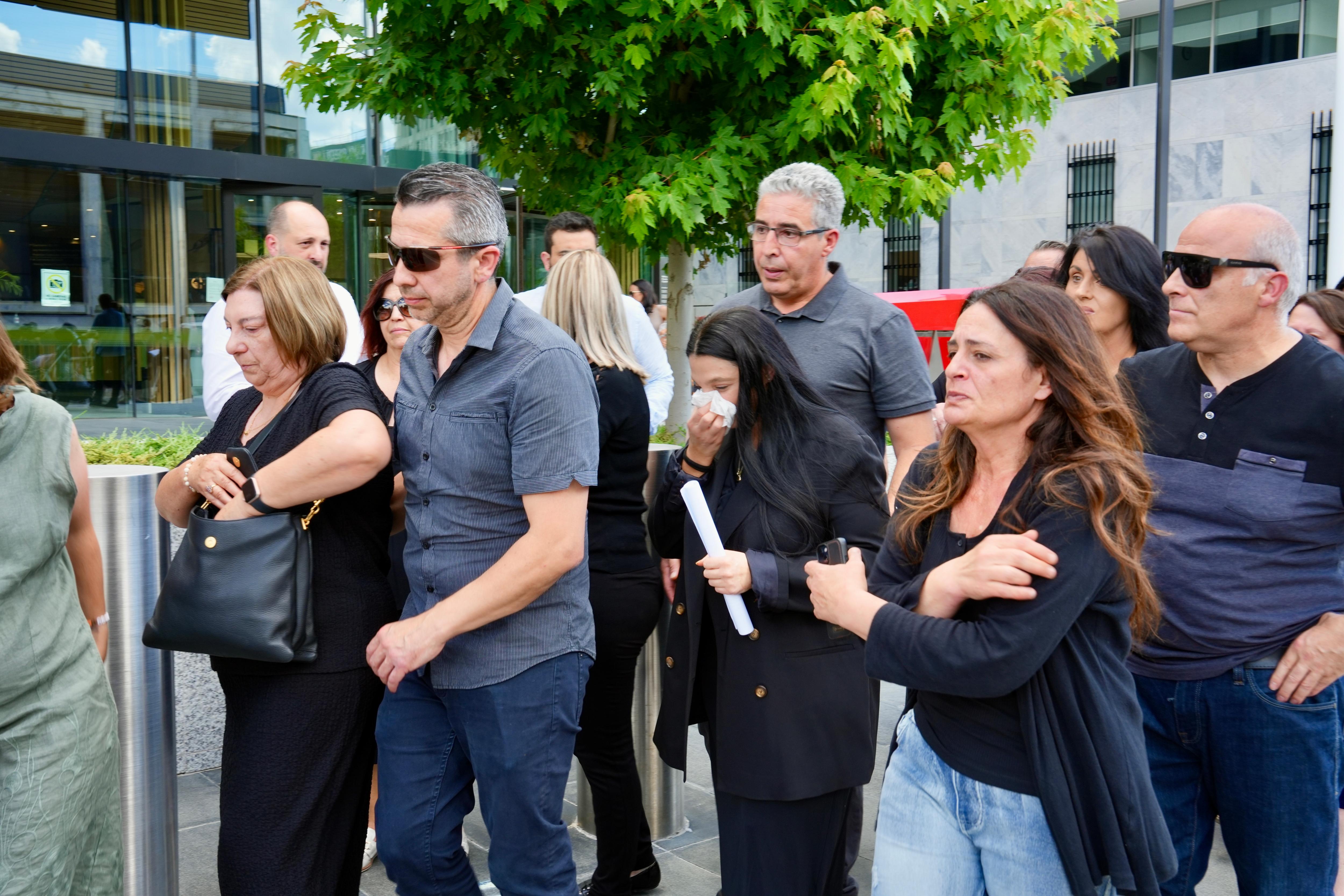 A woman addresses media outside a court, supported by family members and friends.