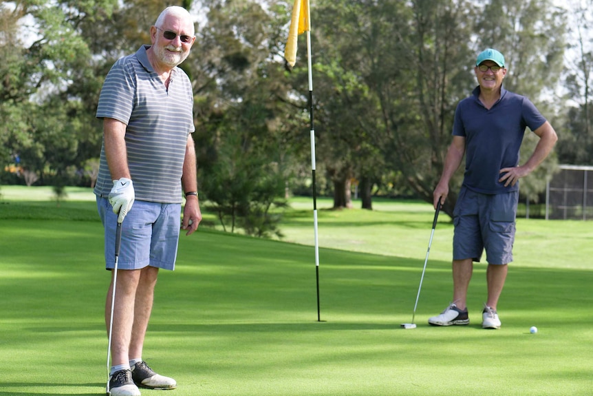 Golfers Andrew Tighe and John Parker stand together on a green at Marrickville Golf Club, April, 2020.